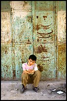 Young boy sitting in front of a closed store, Hebron. West Bank, Occupied Territories (Israel)