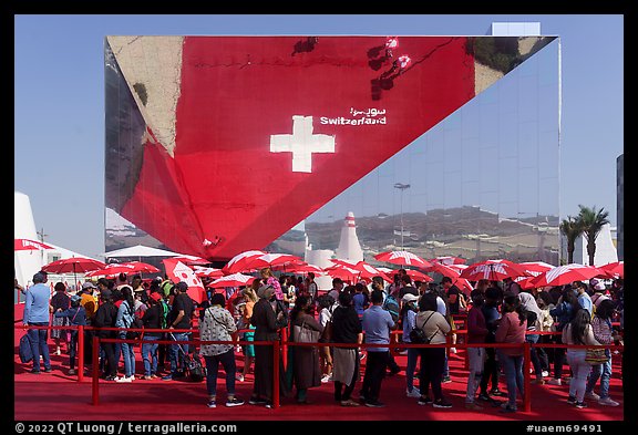 Visitors with umbrellas and reflection, Swizerland Pavilion. Expo 2020, Dubai, United Arab Emirates (color)