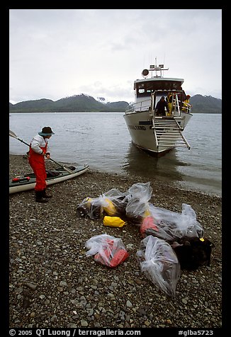 Kayaker standing with gear wrapped in plastic bags after drop-off. Glacier Bay National Park, Alaska (color)