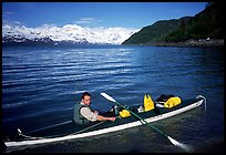Kayaker sitting at a rear of a double kayak with the Fairweather range in the background. Glacier Bay National Park, Alaska
