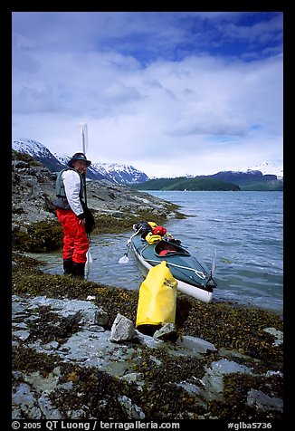 Kayaker standing next to dry bag and kayak on a small island in Muir Inlet. Glacier Bay National Park, Alaska