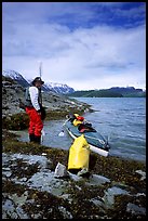 Kayaker standing next to dry bag and kayak on a small island in Muir Inlet. Glacier Bay National Park, Alaska (color)