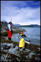 Kayaker standing next to dry bag and kayak on a small island in Muir Inlet. Glacier Bay National Park, Alaska (color)