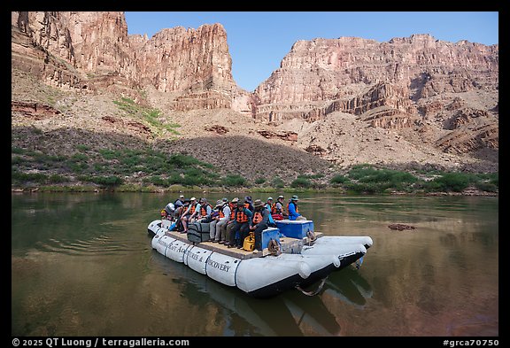 Motorized raft loaded with passengers floats through calm waters of the Colorado River surrounded by towering Grand Canyon cliffs. Grand Canyon National Park, Arizona (color)