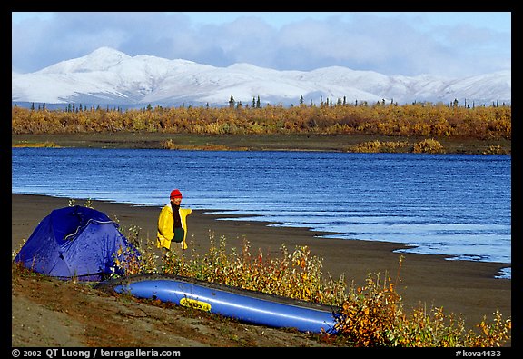 Canoeist standing next to tent and canoe with snowy mountains in the background. Kobuk Valley National Park, Alaska