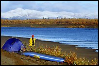 Canoeist standing next to tent and canoe with snowy mountains in the background. Kobuk Valley National Park, Alaska