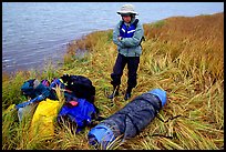 Canoeist standing next to gear and deflated and folded  canoe. Kobuk Valley National Park, Alaska (color)