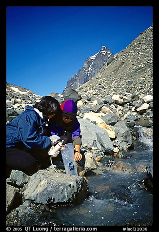 Hikers filing up a water container with a filter. Lake Clark National Park, Alaska