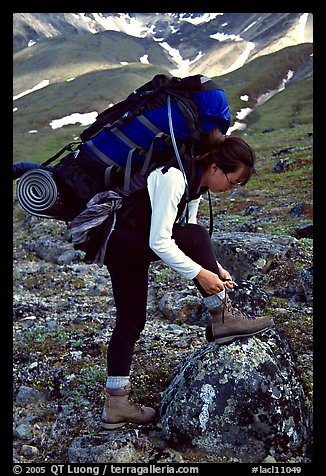 Woman backpacker with a large backpack tying up her shoelaces. Lake Clark National Park, Alaska (color)