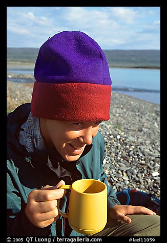 Backpacker drinking from a cup, with mosquitoes on her hat. Lake Clark National Park, Alaska