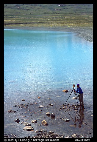 Large format photographer with tripod on the shores of Turquoise Lake. Lake Clark National Park, Alaska