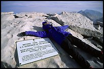 Hiker laying exhausted on Mt Whitney summit sign. California