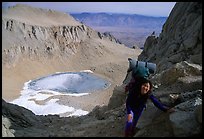 Woman with backpack pausing on steep terrain above Iceberg Lake. California