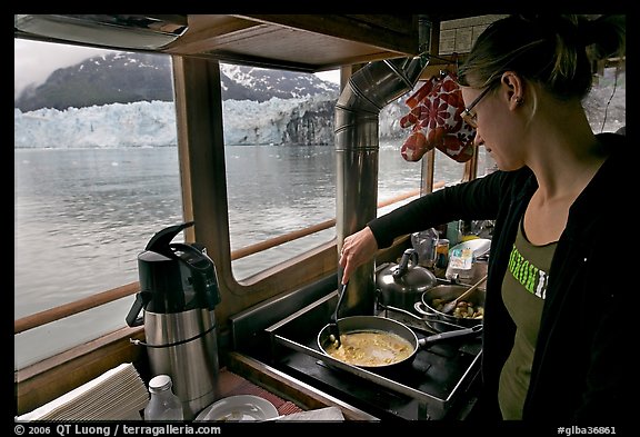 Woman cooking eggs aboard small tour boat, with glacier in view. Glacier Bay National Park, Alaska, USA.