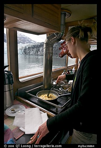 Woman cooking eggs aboard small tour boat, with glacier outside. Glacier Bay National Park (color)