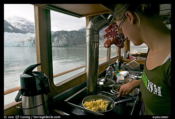 Woman prepares breakfast eggs aboard small tour boat, with glacier in view. Glacier Bay National Park, Alaska, USA.