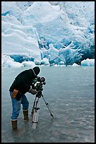 Cameraman standing in water with camera and tripod filming Reid Glacier. Glacier Bay National Park, Alaska, USA.