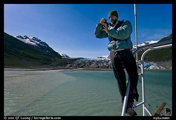 Photographer perched on boat with Reid Glacier behind. Glacier Bay National Park, Alaska, USA.