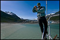 Photographer perched on boat with Reid Glacier behind. Glacier Bay National Park, Alaska, USA.