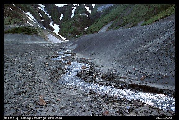 Stream flows from verdant hills into  barren valley floor. Katmai National Park, Alaska, USA.