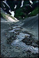 Stream flows from the verdant hills into the barren floor of the Valley of Ten Thousand smokes. Katmai National Park, Alaska, USA. (color)