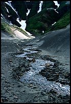 Stream flows from the verdant hills into the barren floor of the Valley of Ten Thousand smokes. Katmai National Park, Alaska, USA.