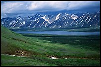 Verdant tundra, lake, and snowy mountains under clouds. Lake Clark National Park, Alaska, USA.