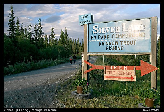 Sign and couple walking on McCarthy road near Silver Lake. Wrangell-St Elias National Park, Alaska, USA.