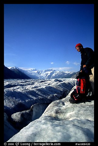 Hiker reaches for item in backpack on Root Glacier. Wrangell-St Elias National Park, Alaska, USA.