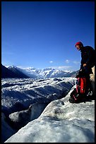 Hiker reaches for item in backpack on Root Glacier. Wrangell-St Elias National Park, Alaska, USA.