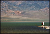 Two tourists on shore of rare lake on the floor of the Valley. Death Valley National Park, California, USA.