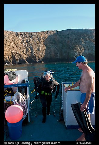 Woman diver stepping onto boat and Annacapa Island. Channel Islands National Park, California, USA.