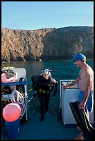 Woman diver stepping onto boat and Annacapa Island. Channel Islands National Park, California, USA.