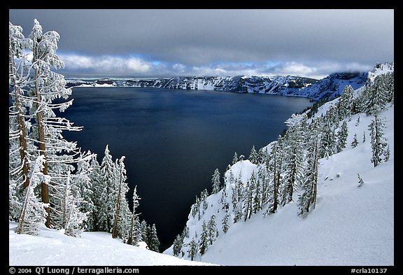 Trees and lake in winter with clouds and dark waters. Crater Lake National Park, Oregon, USA.