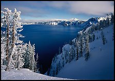 Snow-covered trees and dark lake waters. Crater Lake National Park, Oregon, USA.