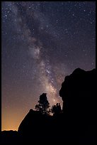 Rocks and pine trees profiled against starry sky with Milky Way. Pinnacles National Park, California, USA.