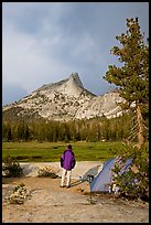 Camper standing next to tent looks at Cathedral Peak, evening. Yosemite National Park, California, USA.