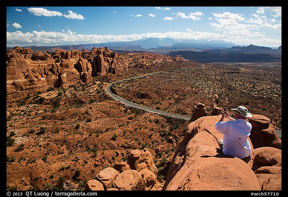 Tourist taking picture from top of fin. Arches National Park, Utah, USA.