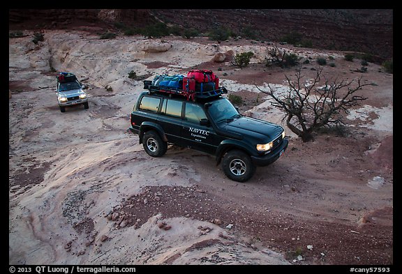 4WD vehicles driving over rock at dusk in Teapot Canyon. Canyonlands National Park, Utah, USA.