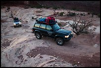 4WD vehicles driving over rock at dusk in Teapot Canyon. Canyonlands National Park, Utah, USA.