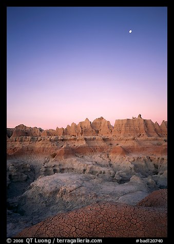 Mud cracks, badlands, and moon at dawn. Badlands National Park, South Dakota, USA.