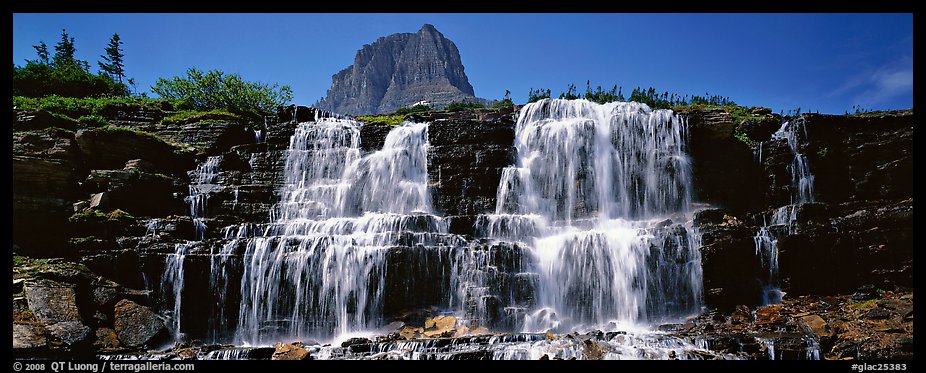 Waterfall flowing over dark rock and peak. Glacier National Park (color)