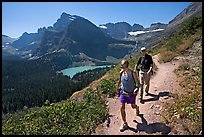 Couple hiking on trail, with Grinnell Lake below. Glacier National Park, Montana, USA.