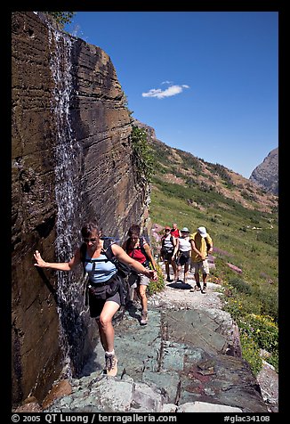 Walking under a small waterfall on the Grinnell Glacier trail. Glacier National Park, Montana, USA.