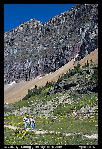 Couple hiking on trail amongst wildflowers near Hidden Lake. Glacier National Park, Montana, USA.