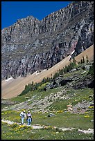 Couple hiking on trail amongst wildflowers near Hidden Lake. Glacier National Park, Montana, USA.