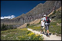 Hikers on trail amongst wildflowers near Hidden Lake. Glacier National Park, Montana, USA. (color)