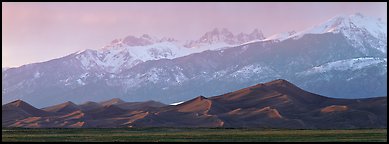 Sand dunes below snowy mountain range at sunset. Great Sand Dunes National Park and Preserve (Panoramic color)