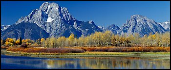 Rugged mountains rising above tree-lined lake in autumn. Grand Teton National Park (Panoramic color)