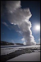 Old Faithful Geyser in the winter with moon. Yellowstone National Park, Wyoming, USA.